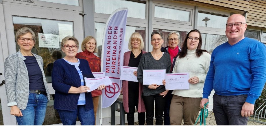 Gruppenfoto der neuen Bürgerhelfer*innen, Koordinatorin Sabine Bodenbender und Bürgermeister Dr. Jens Ried vor dem EIngang der Gemeindehalle Cölbe